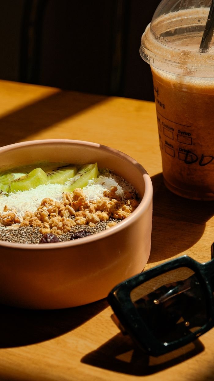 Fresh kiwi breakfast bowl with granola and chia seeds served with iced coffee on a sunny morning.