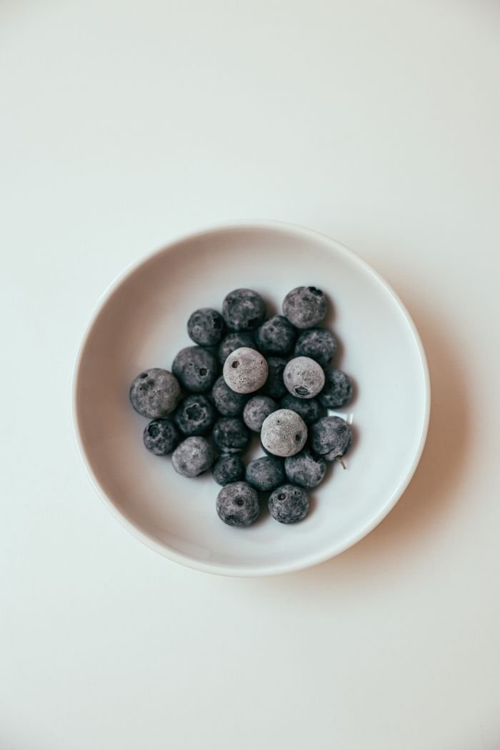 Close-up of fresh blueberries arranged in a white ceramic bowl on a neutral background.